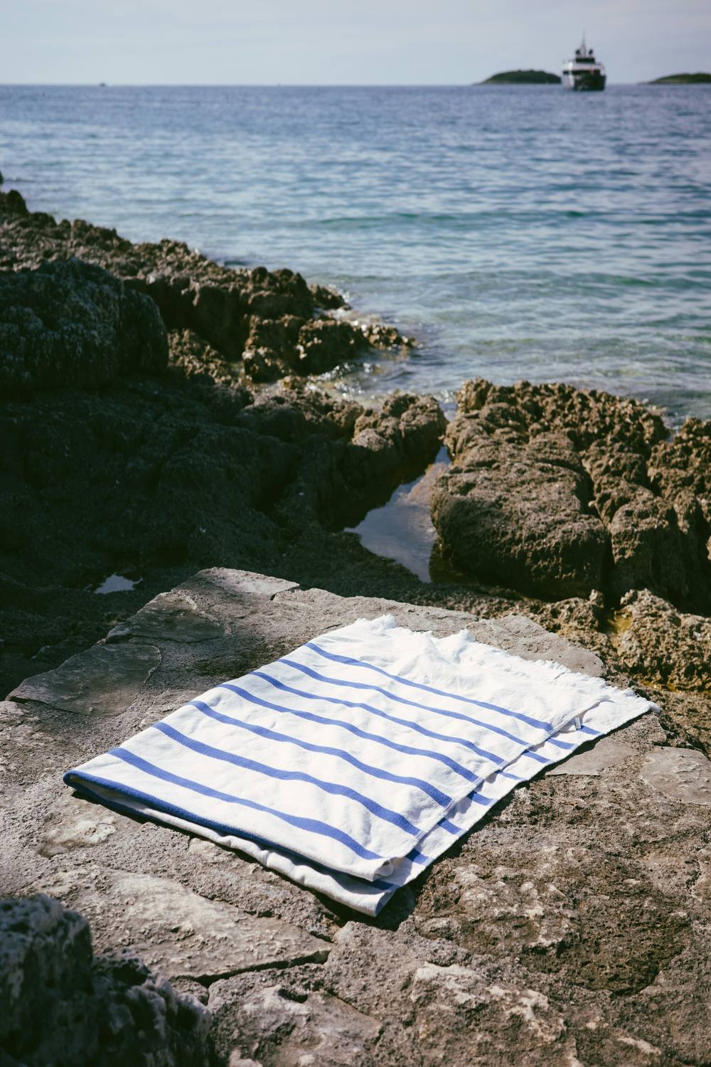 Toalla plana de rayas azules sobre las rocas, junto al mar