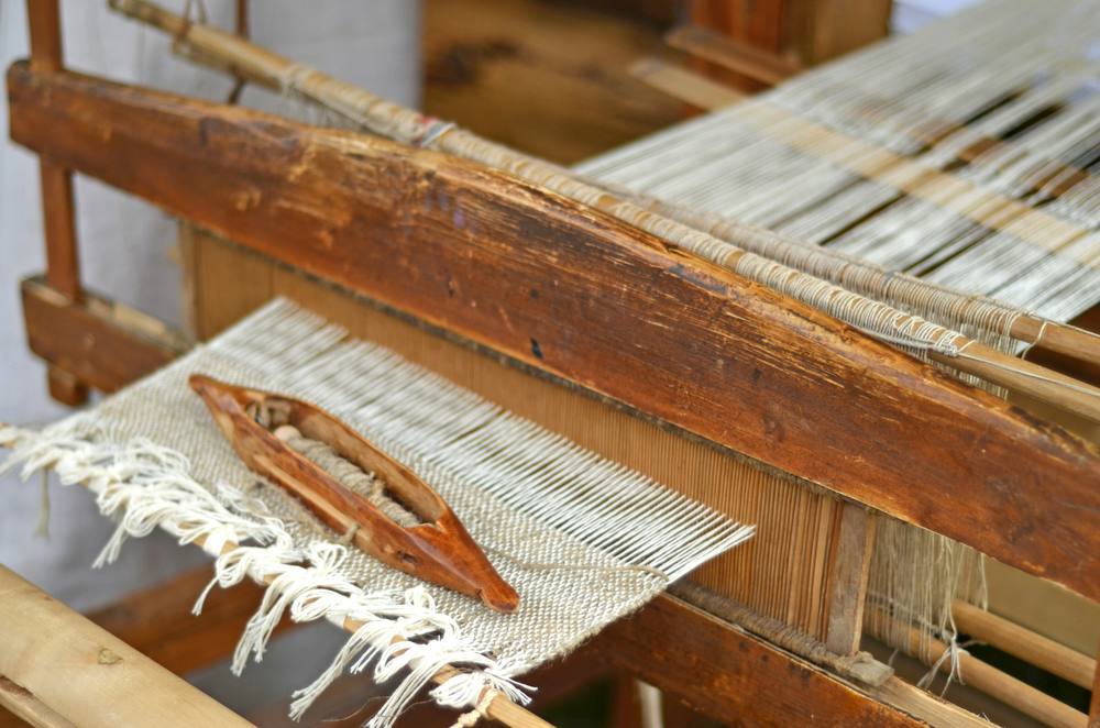Telar tradicional de madera con su lanzadera y un tejido con flecos